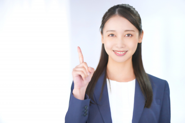 指を立てて微笑むスーツ姿の女性